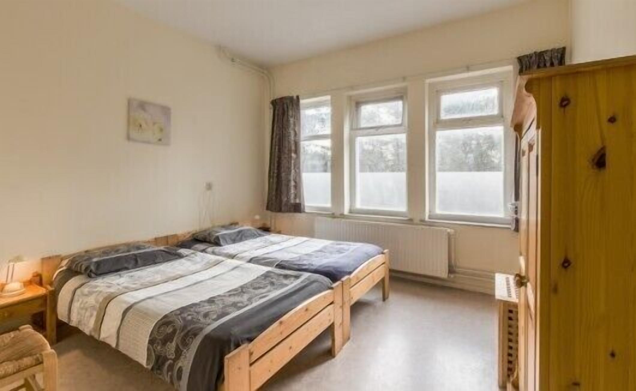 Un dormitorio con dos camas, un armario de madera, un radiador y una ventana con cortinas.