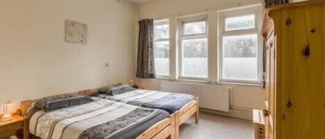 Un dormitorio con dos camas, un armario de madera, un radiador y una ventana con cortinas.