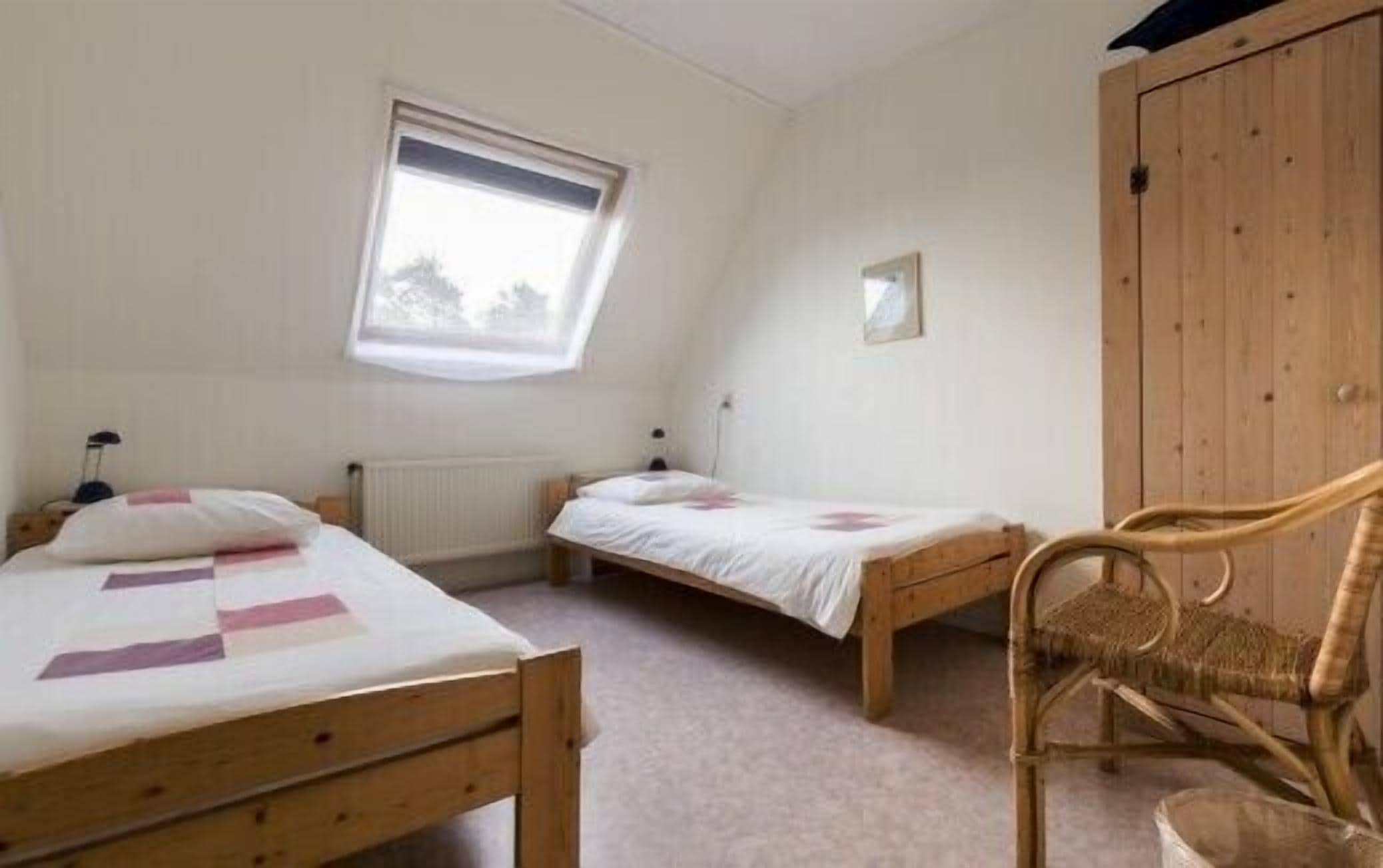 Un dormitorio con dos camas de madera, una ventana, un radiador y un armario de madera.