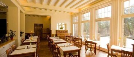 A dining area with multiple tables and chairs, large windows, and a wooden ceiling.