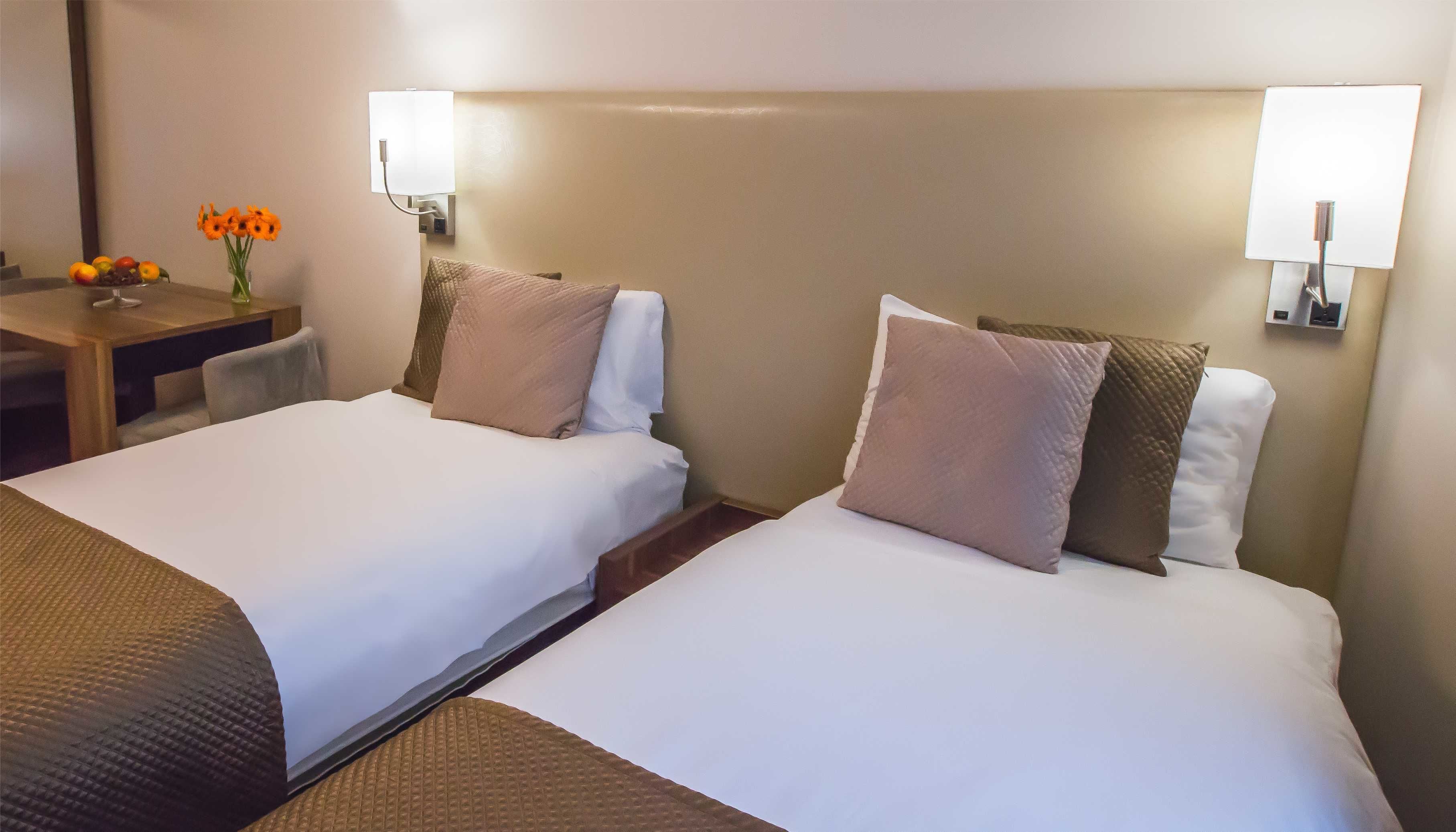 Una habitación de hotel con dos camas, un escritorio y un florero.
