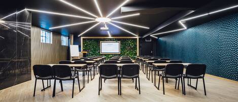 A conference room with a modern design, featuring a long table with chairs, a projector screen, and a green wall with a textured pattern.
