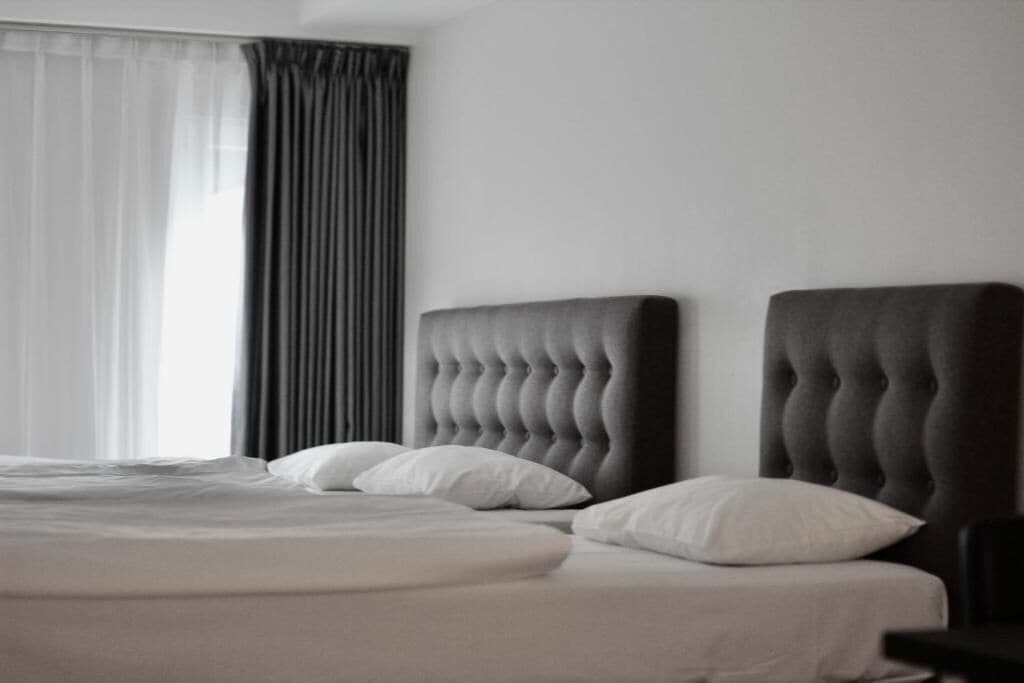A bedroom with a large bed, dark headboard, and a window with sheer curtains.