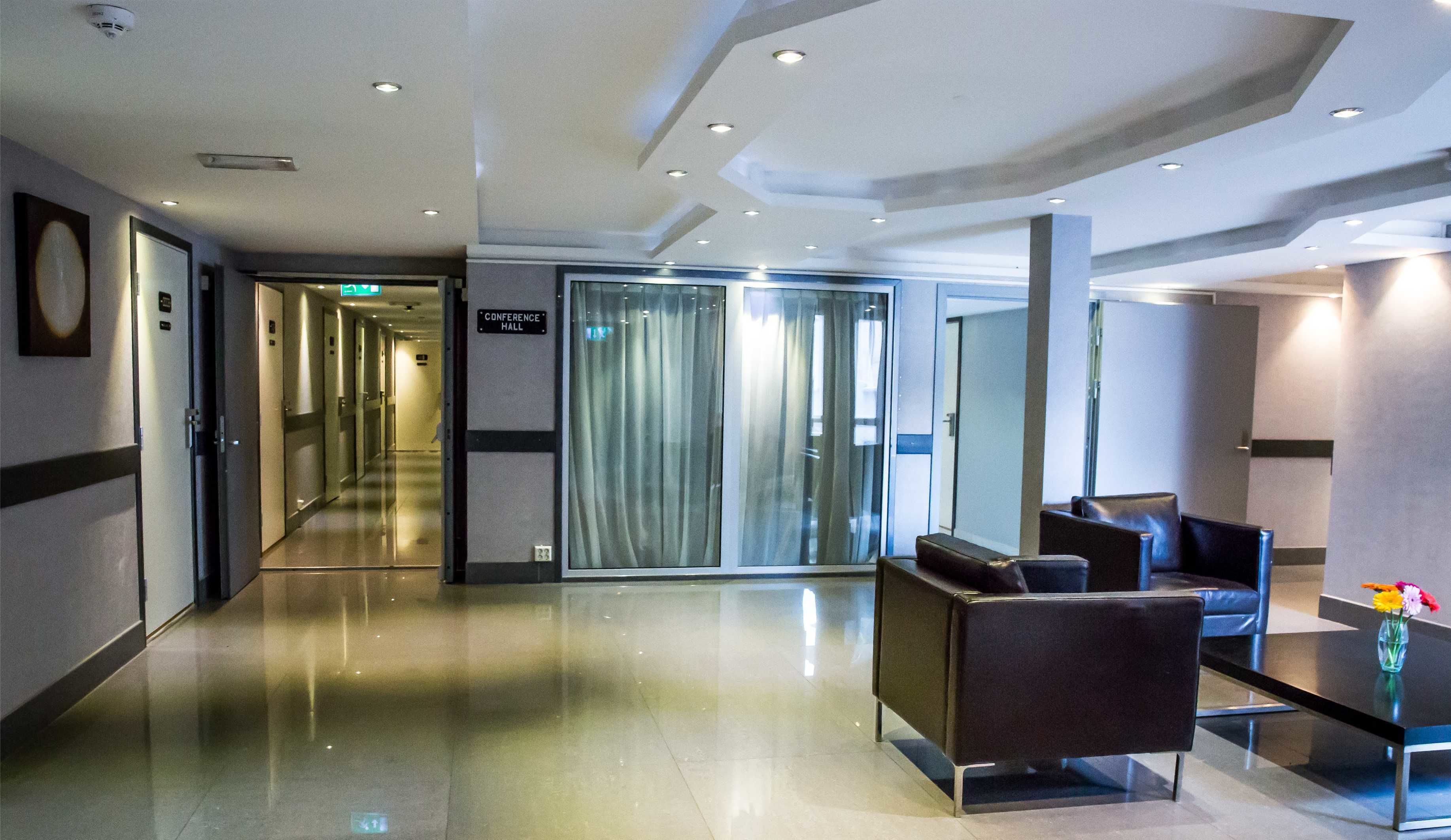 A modern hotel lobby with a long corridor, a conference hall, and seating area with a vase of flowers.