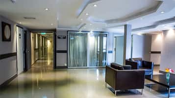 A modern hotel lobby with a long corridor, a conference hall, and seating area with a vase of flowers.