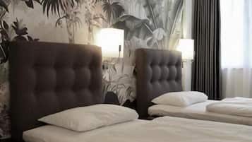 A hotel room with a large bed, two bedside tables, a wall mural, and a window with curtains.