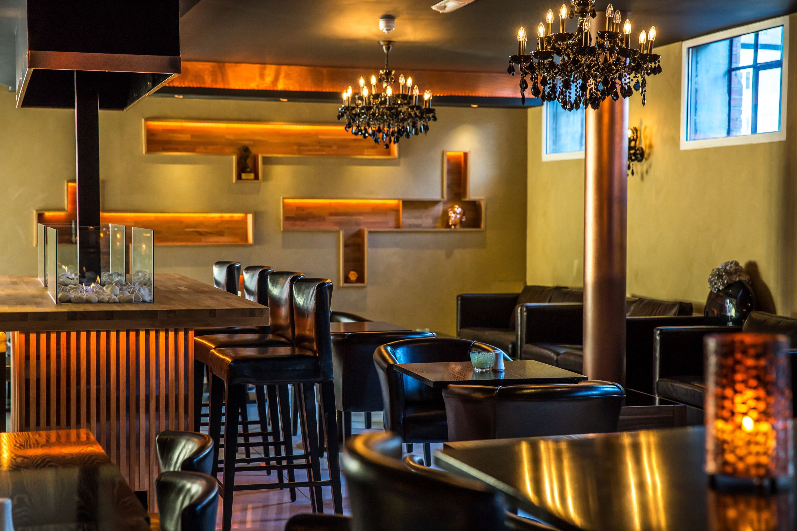 A restaurant interior with a bar area, seating, and a chandelier.
