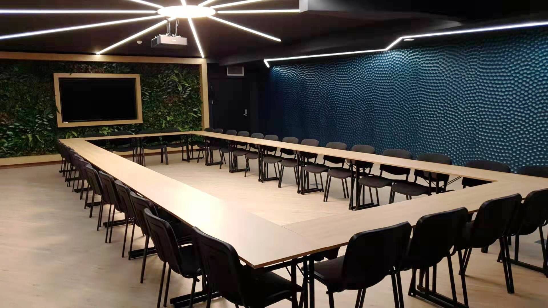 Un salón de conferencias con una larga mesa y sillas, una pantalla de proyector y una pared insonorizada.