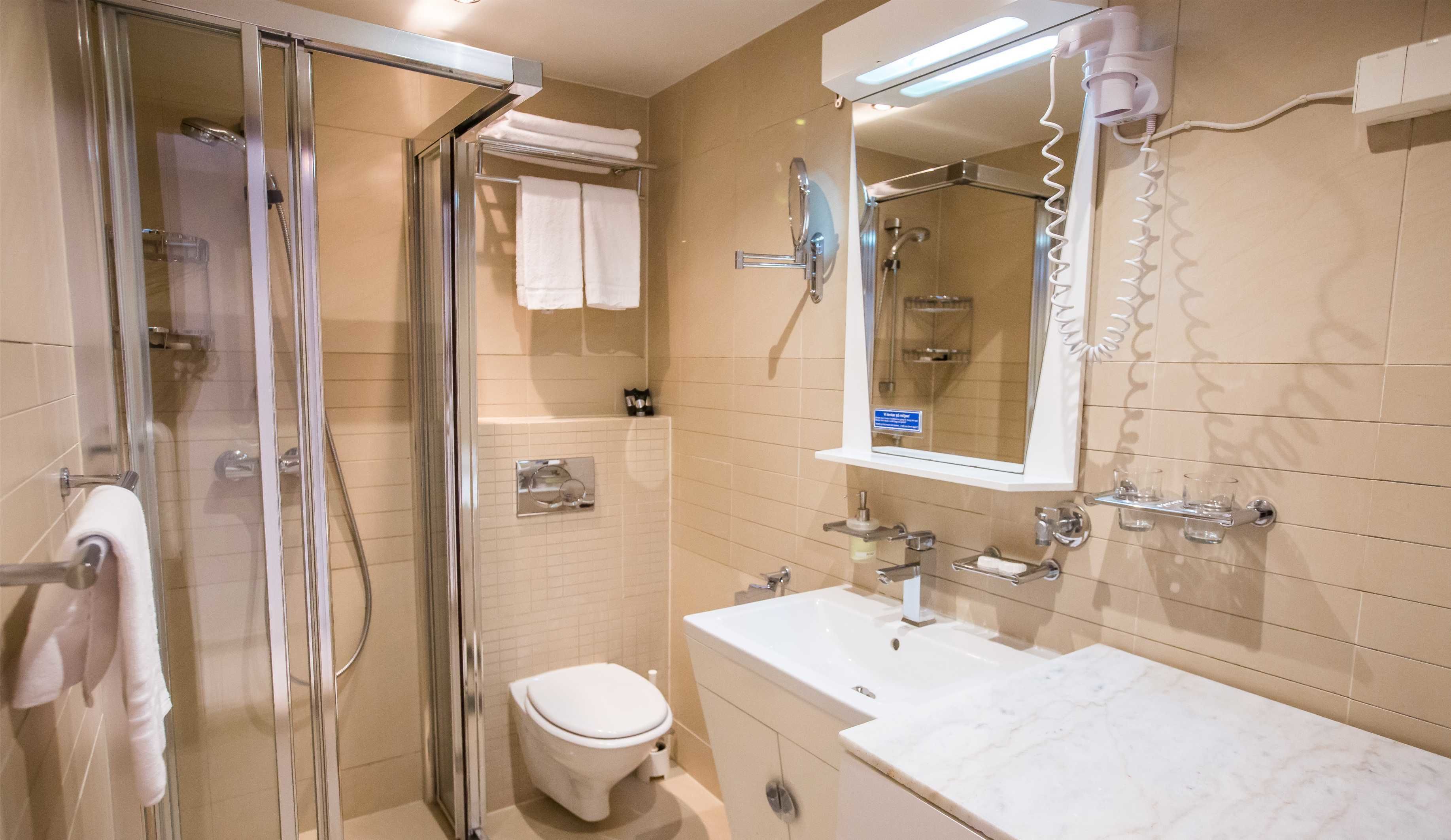 Een moderne badkamer met een glazen douchecabine, een wit toilet, een wastafel met spiegel en een handdoekhouder.