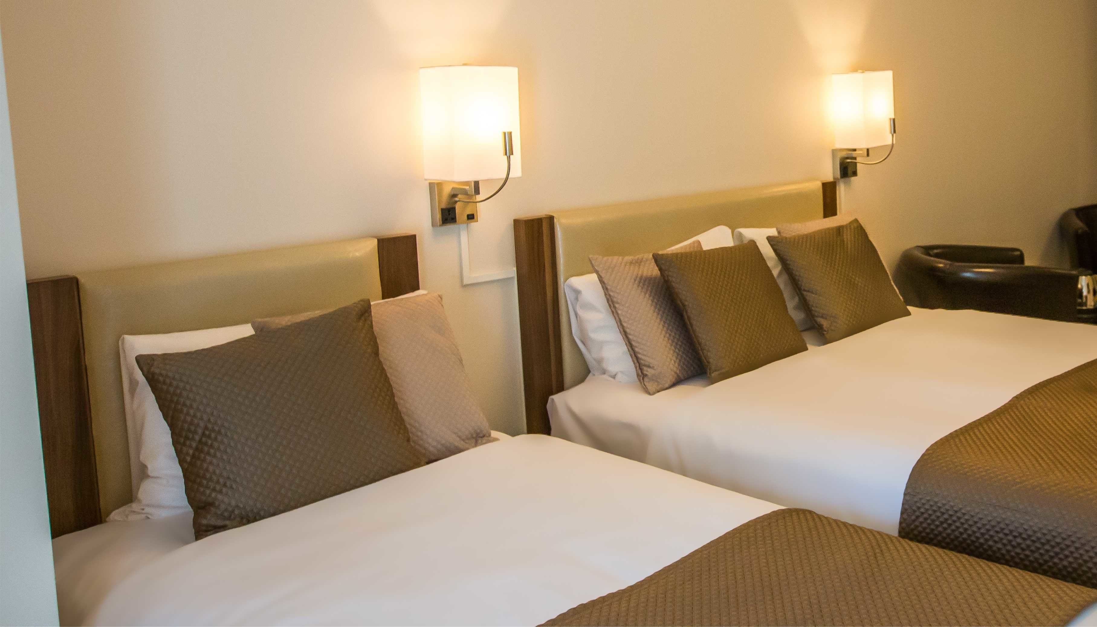 Two beds with headboards, each with a wall-mounted lamp.