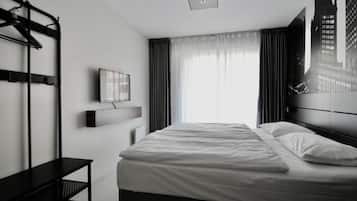 A modern hotel room with a bed, a TV mounted on the wall, a bench, and a window with curtains.