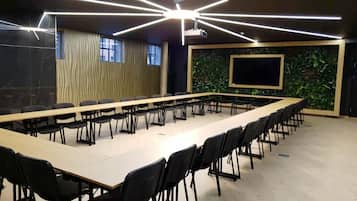 A conference room with a long table, black chairs, a projector screen, and a green wall with plants.