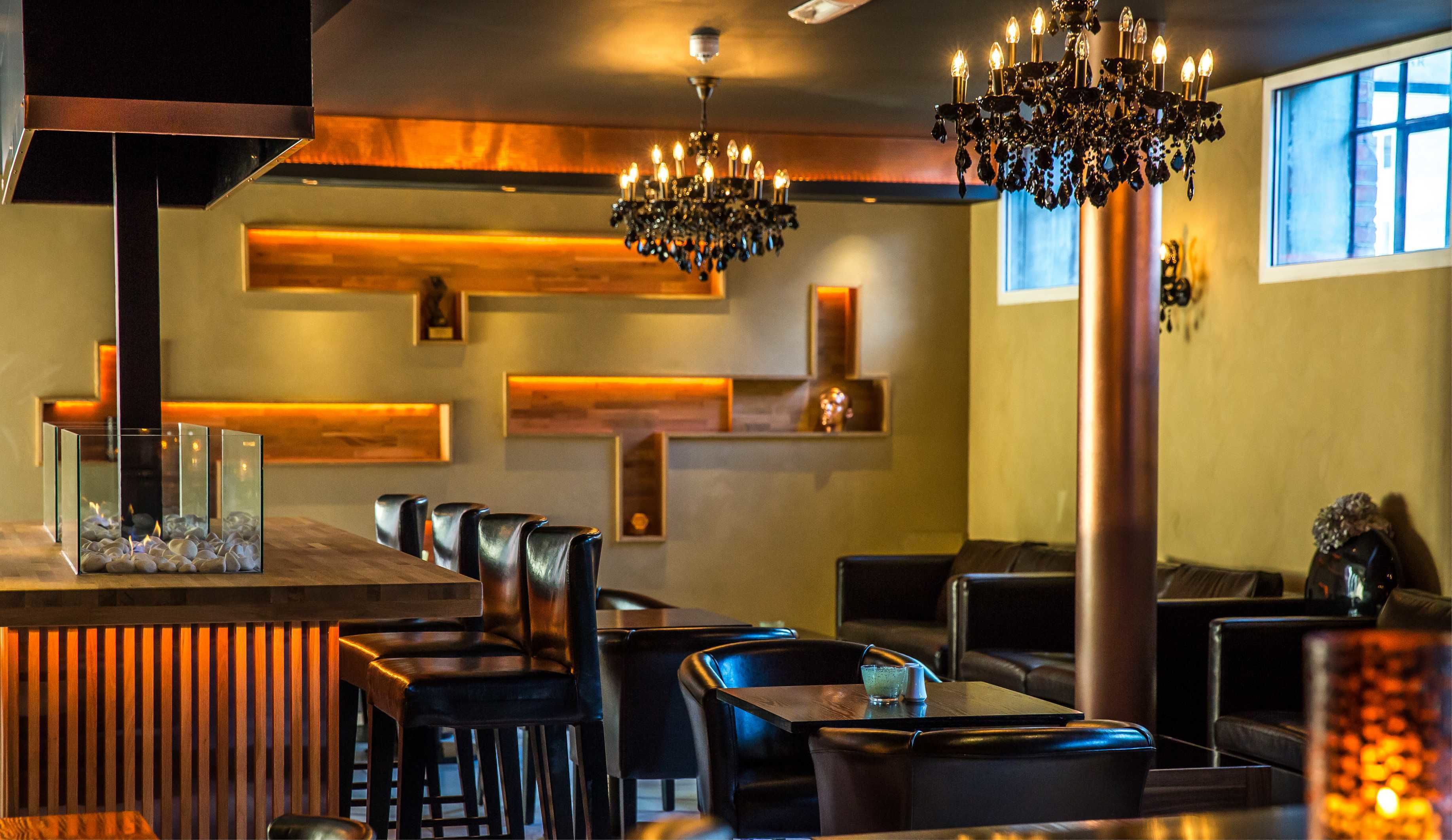A restaurant interior with a bar area, leather seating, and a decorative chandelier.