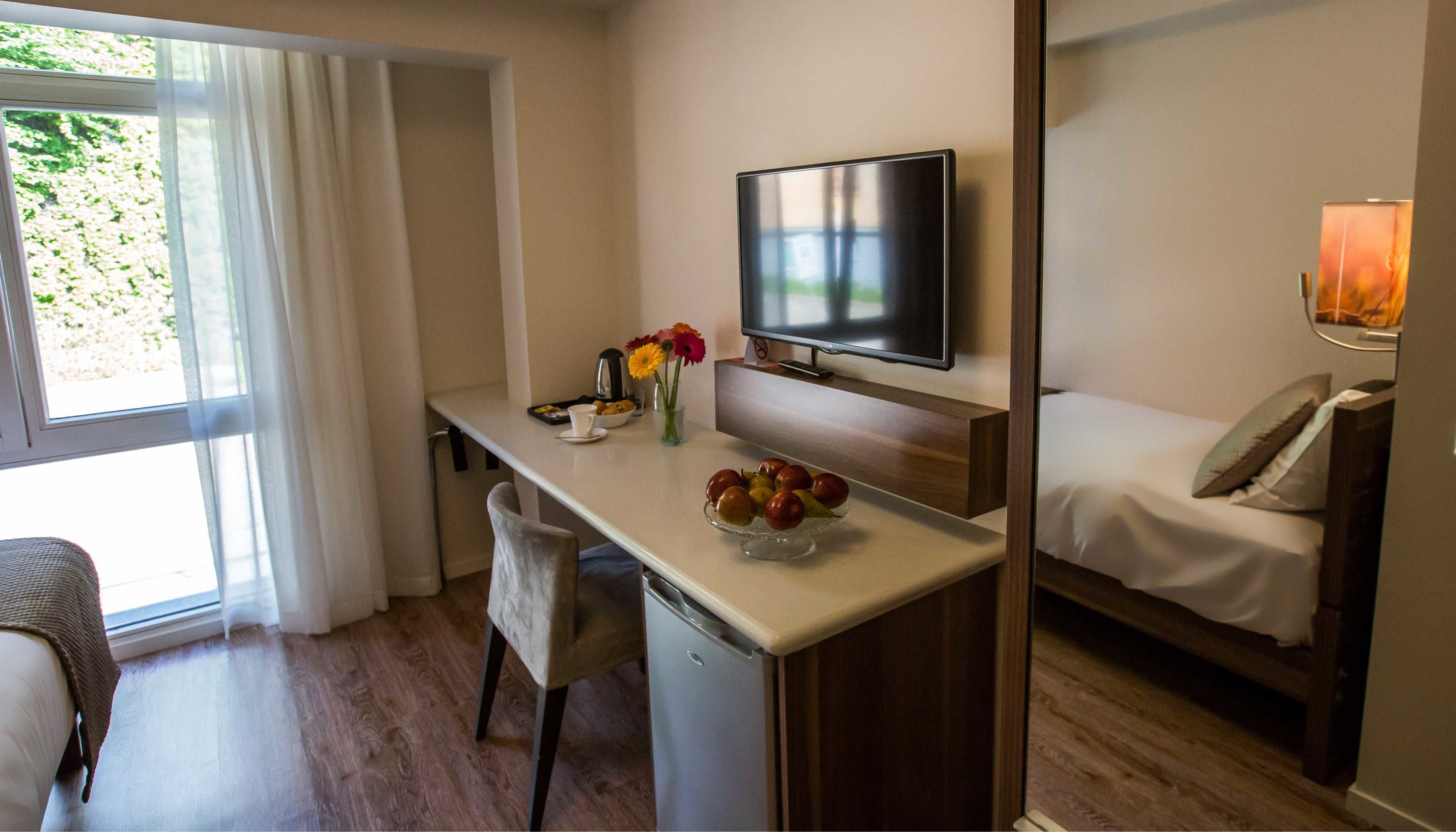 Una habitación de hotel compacta con kitchenette, una cama, un televisor y un ventanal con cortinas.