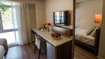 Una habitación de hotel compacta con kitchenette, una cama, un televisor y un ventanal con cortinas.