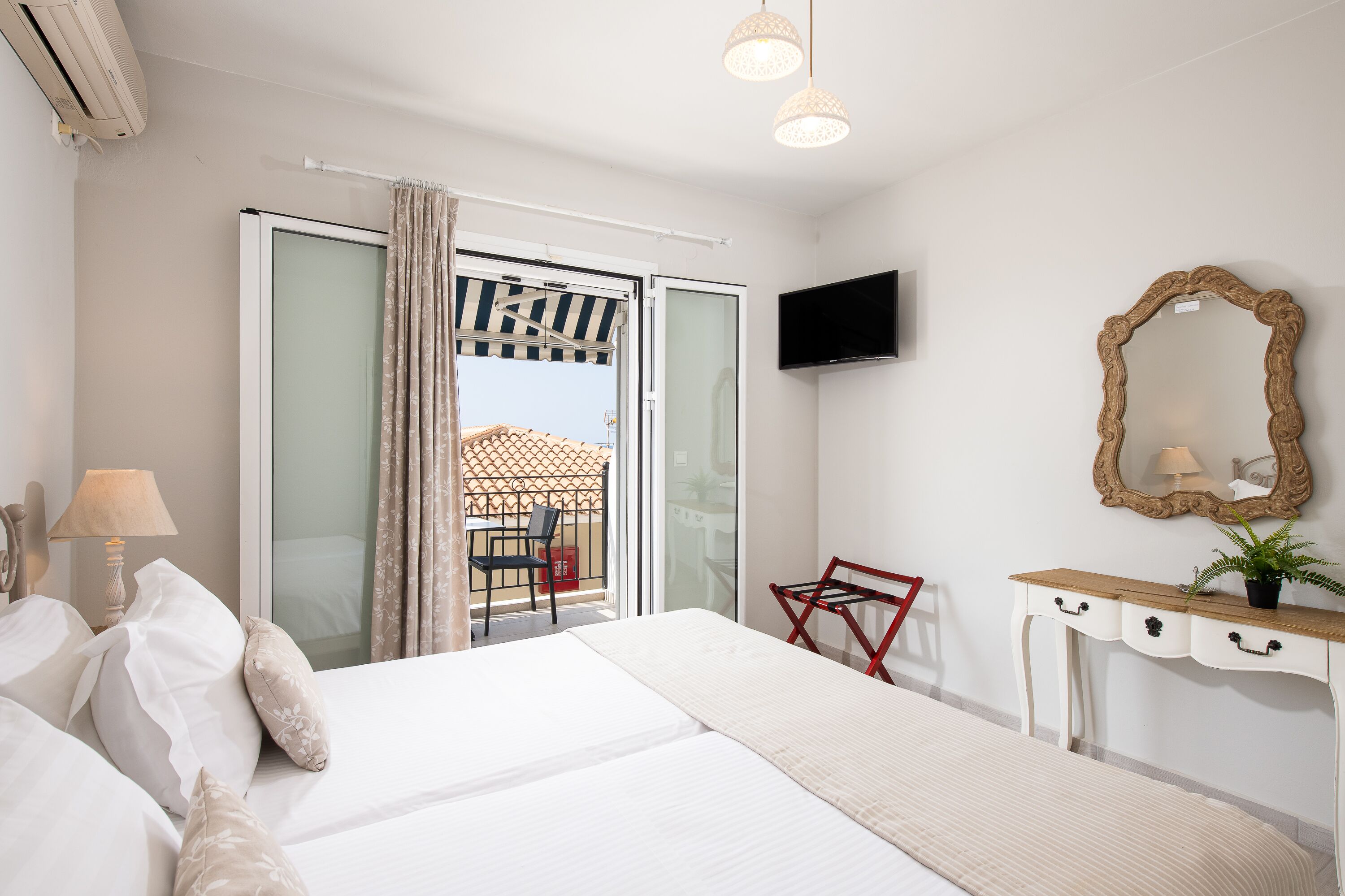 A hotel room with a bed, a desk with drawers, a TV mounted on the wall, and a balcony with a chair and umbrella.