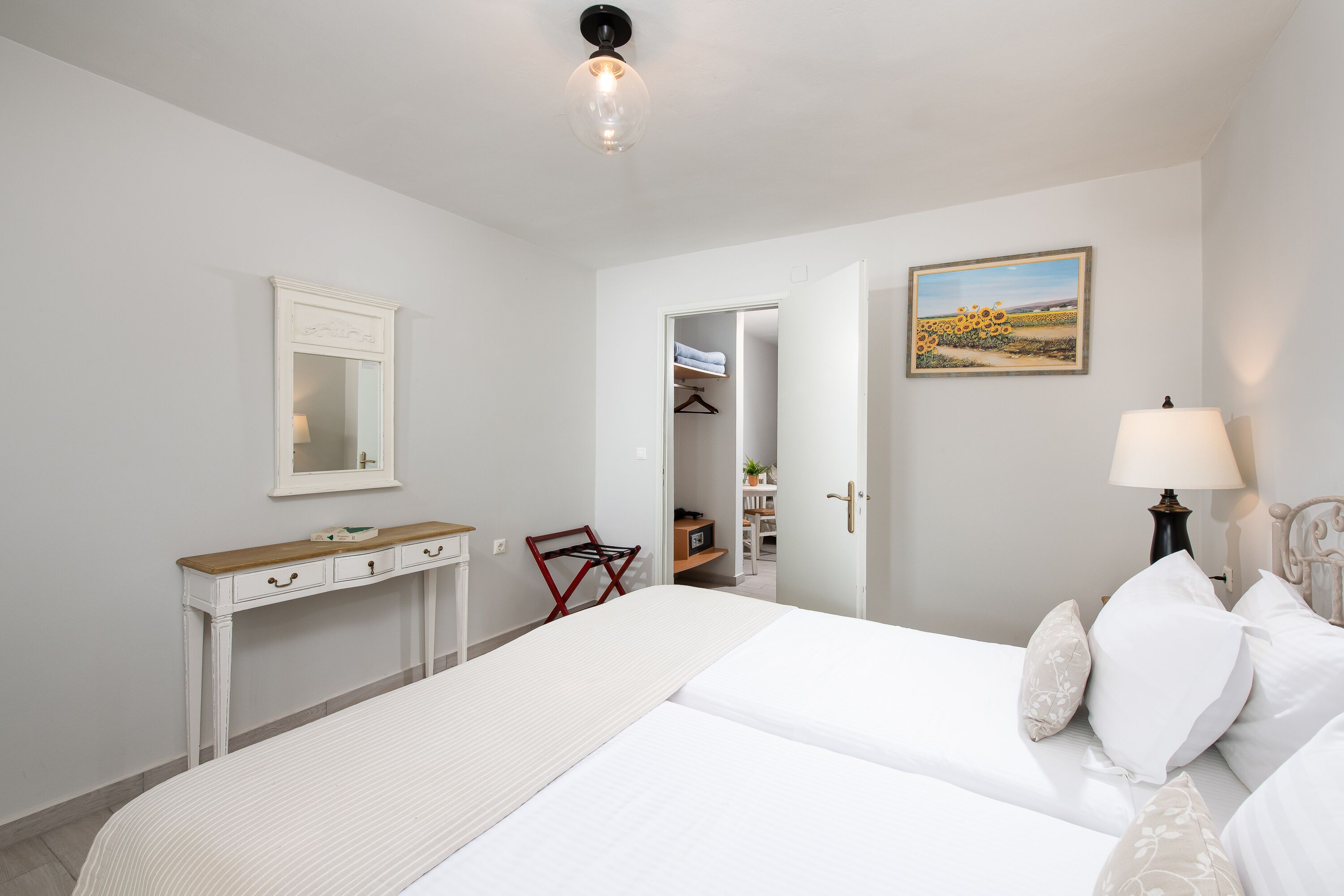 A bedroom with a bed, bedside table, mirror, and a painting on the wall.