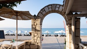 Un arco de piedra que da paso a una playa con sombrillas y sillas reclinables.