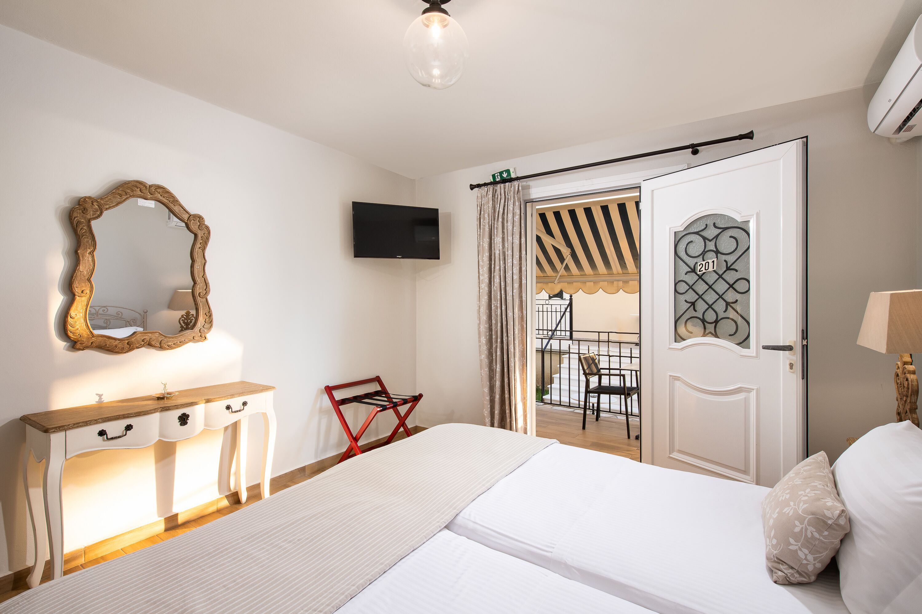 Ein Schlafzimmer mit Bett, Schminktisch, Fernseher und einer Tür, die auf einen Balkon führt.