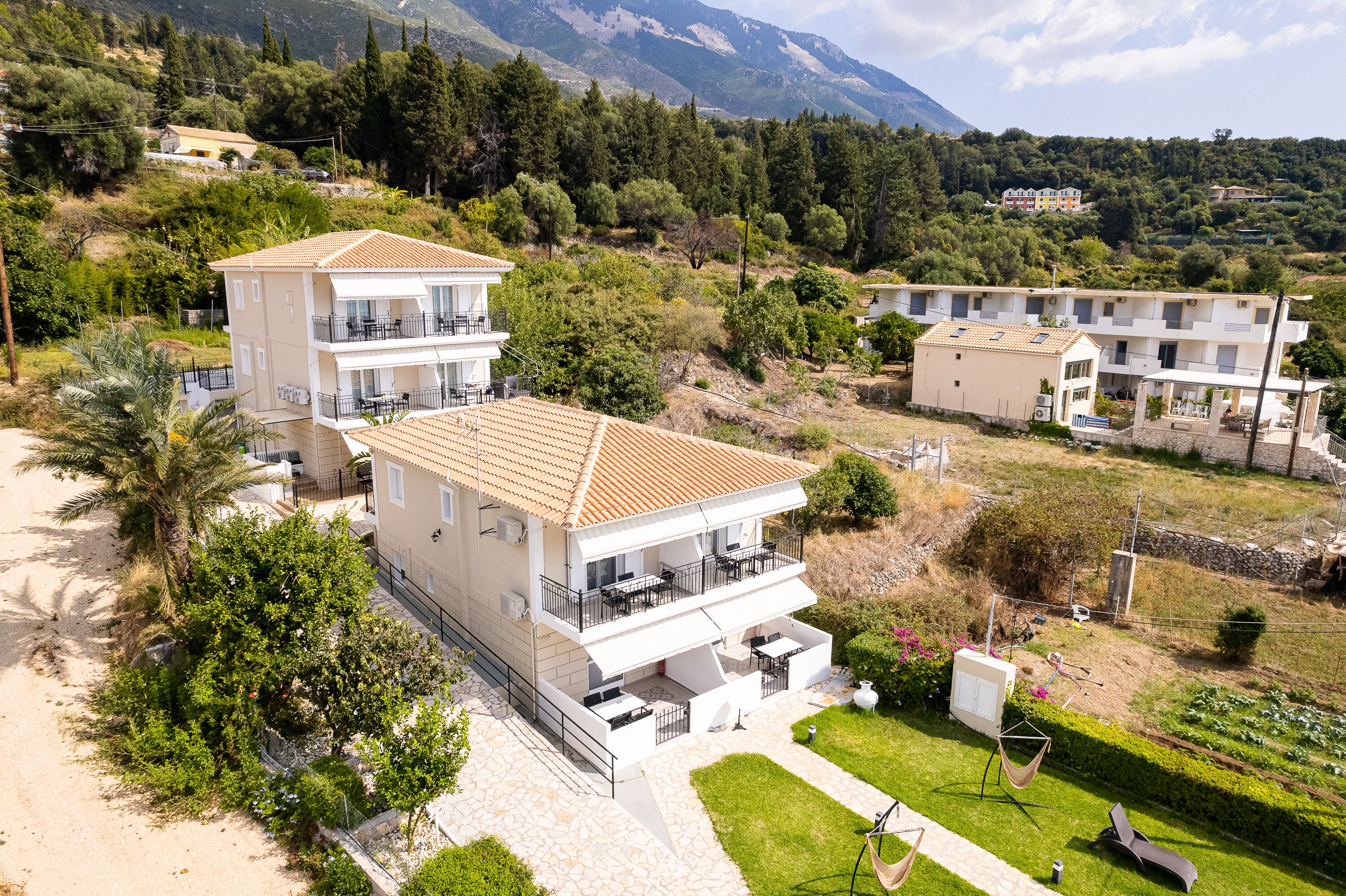 A two-story building with balconies, a garden, and a view of the surrounding landscape.