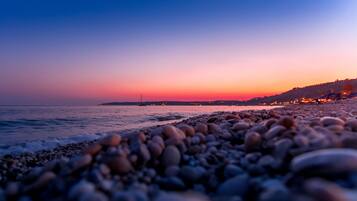 A beach with pebbles in the foreground and a sunset in the background.