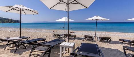A beach with sun loungers and umbrellas, a clear blue sky, and calm sea.