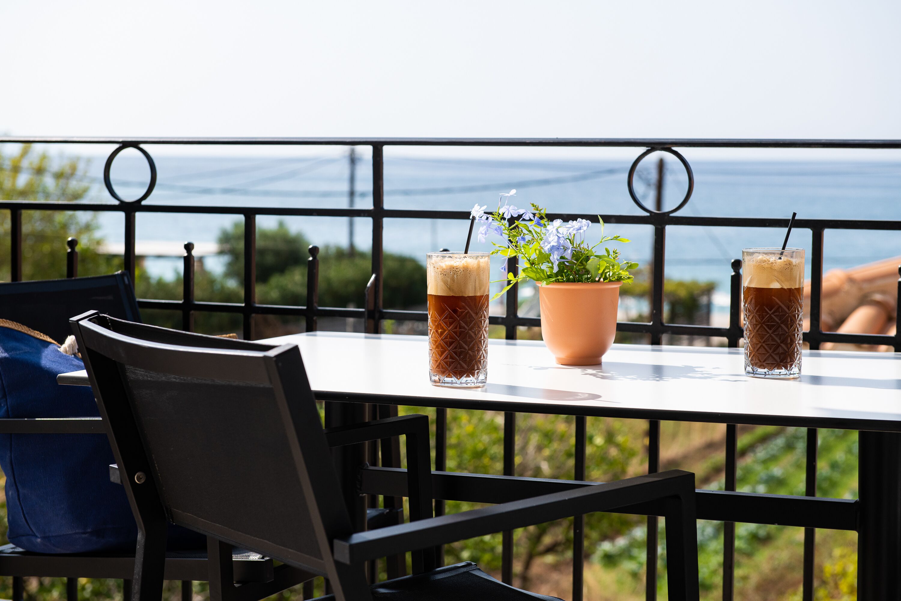 Une table avec deux verres de café glacé, une plante en pot et une chaise avec un coussin bleu.