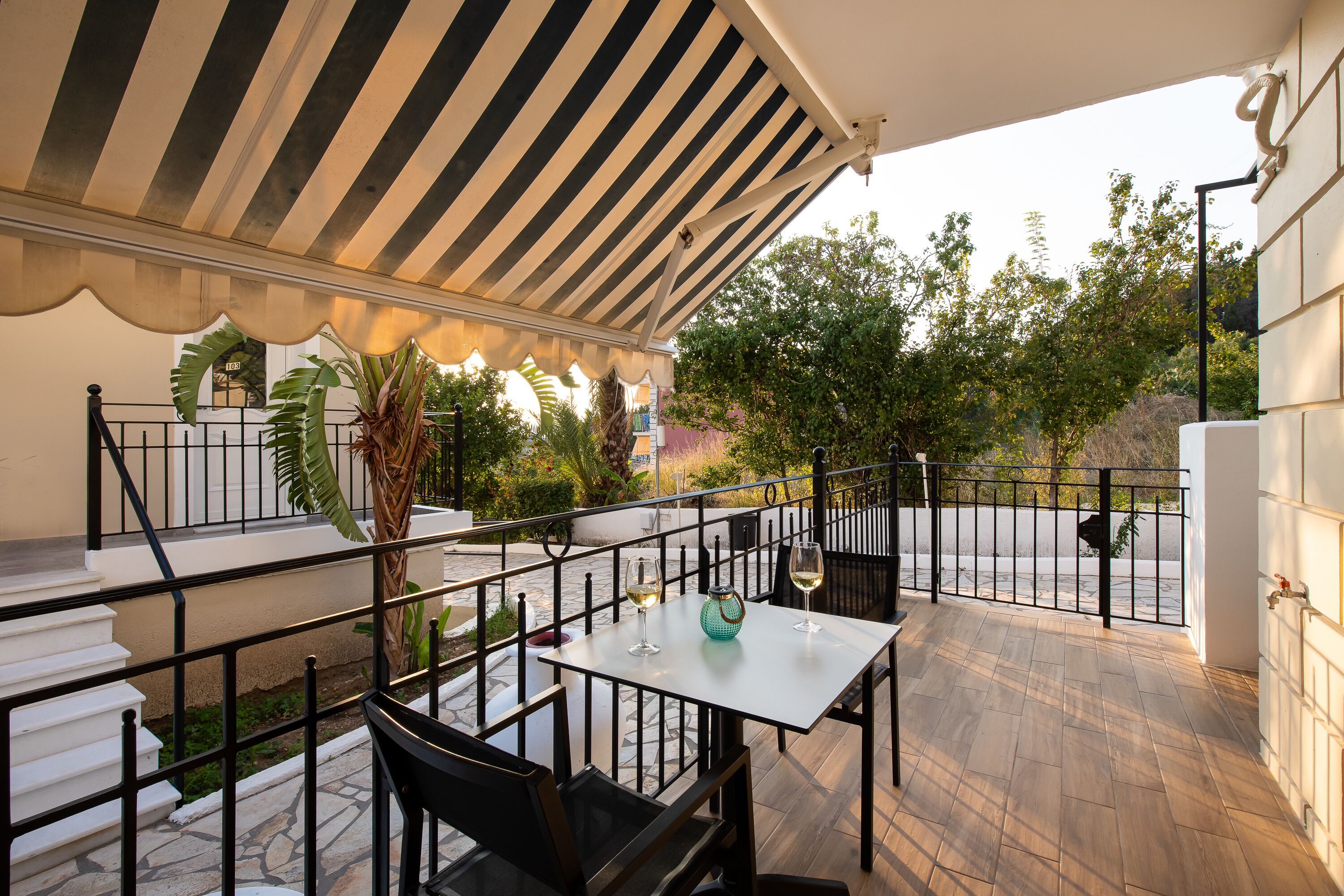 An outdoor patio with a striped awning, a table with chairs, and a railing.