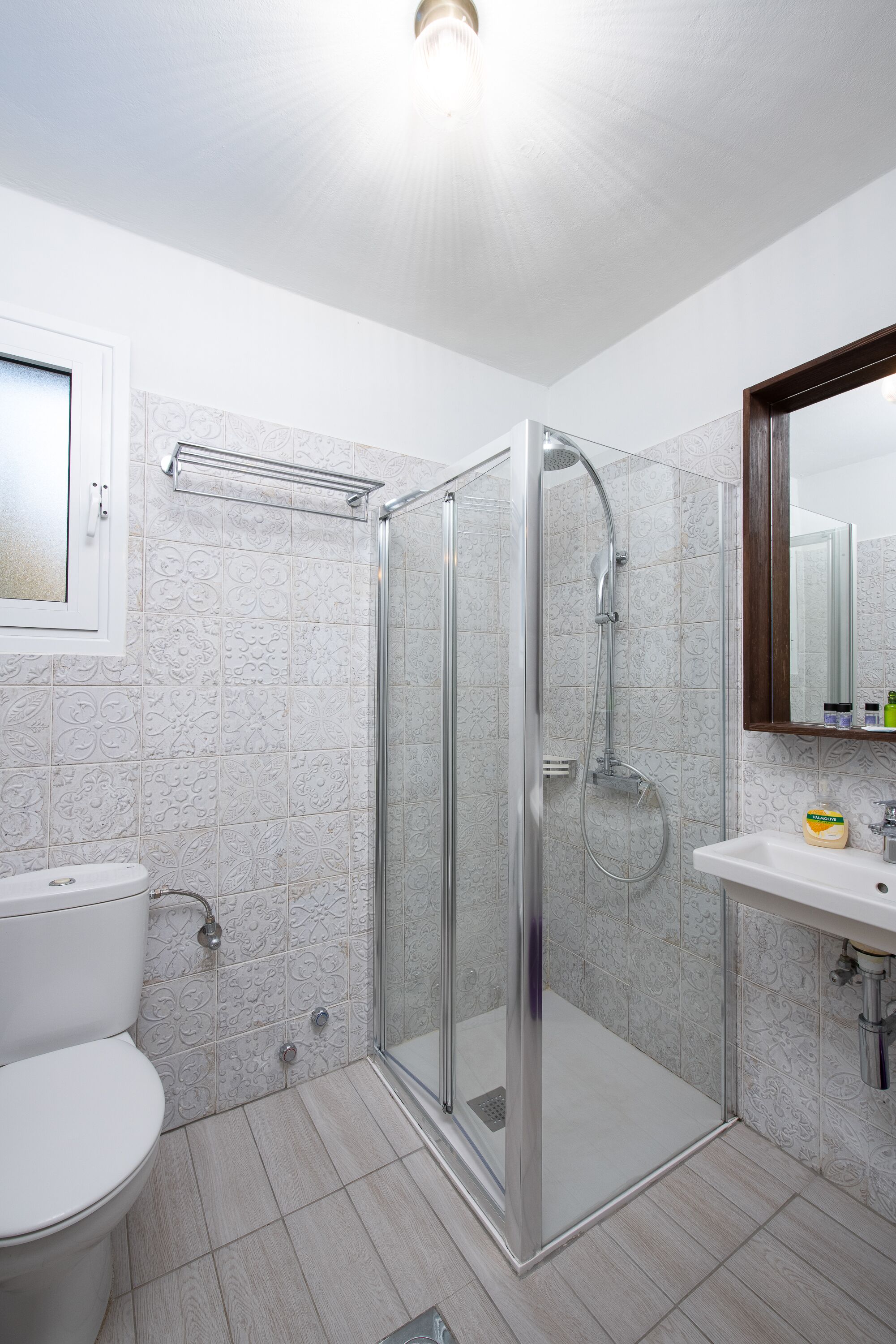 Un baño moderno con ducha de vidrio, inodoro blanco y lavamanos con espejo.
