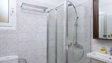 A modern bathroom with a glass-enclosed shower, a white toilet, and a sink with a mirror above it.