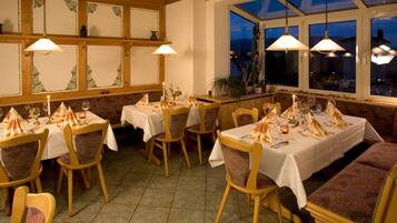 Ein Restaurant mit mehreren gedeckten Tischen, Holzstühlen und hängenden Pendelleuchten.