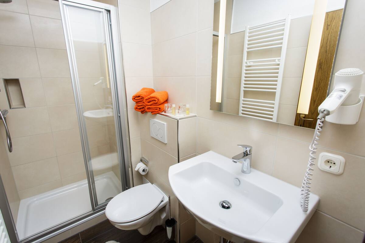 A bathroom with a shower, toilet, sink, and a hairdryer on the wall.