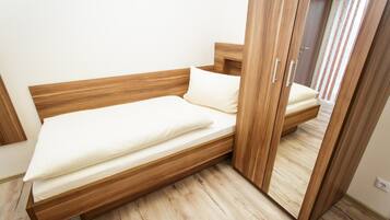 A single bed with a wooden frame and white bedding in a room with light wooden flooring and a wooden wardrobe.