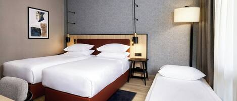 A hotel room with two beds, a desk, a chair, a lamp, and a framed picture on the wall.