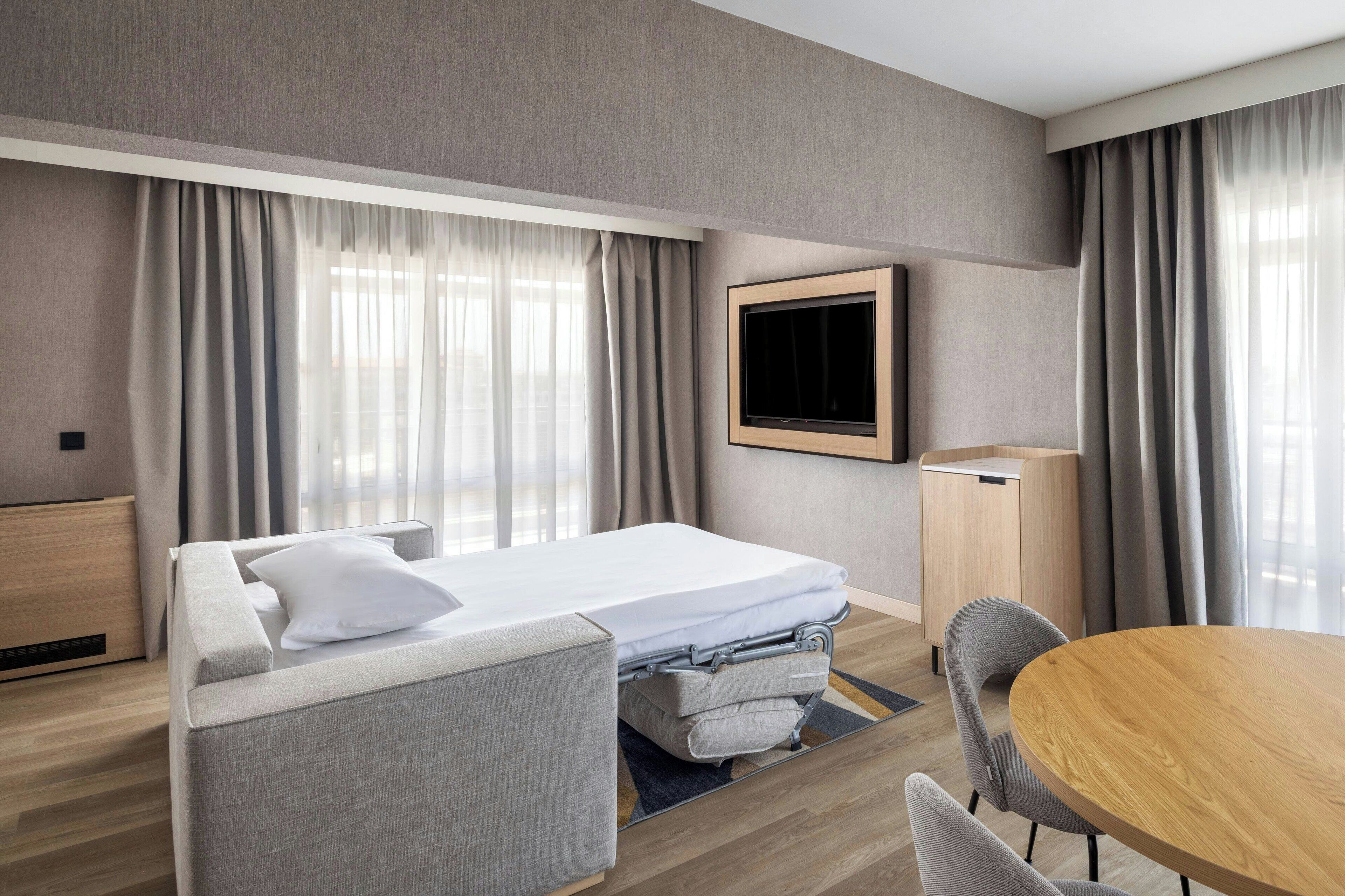 Ett modernt hotellrum med en säng, ett skrivbord, en stol och en tv.