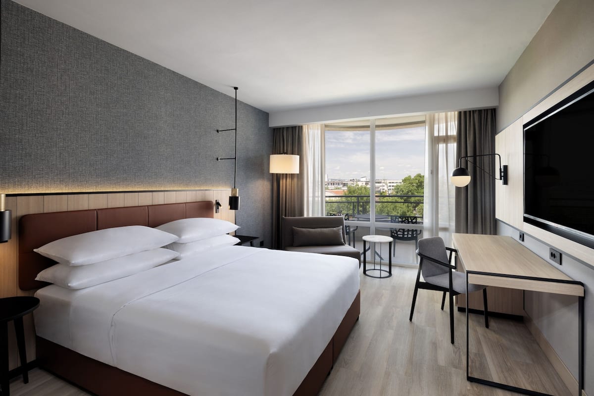 Une chambre d’hôtel moderne dotée d’un grand lit, d’un bureau, d’une chaise, d’une télévision et d’un balcon avec vue.