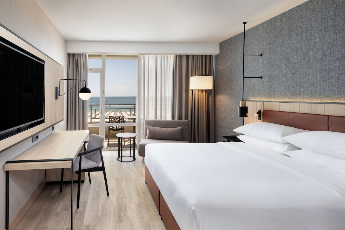 Une chambre d’hôtel équipée d’un lit, d’un bureau, d’une chaise, d’une télévision et offrant une vue sur la plage.