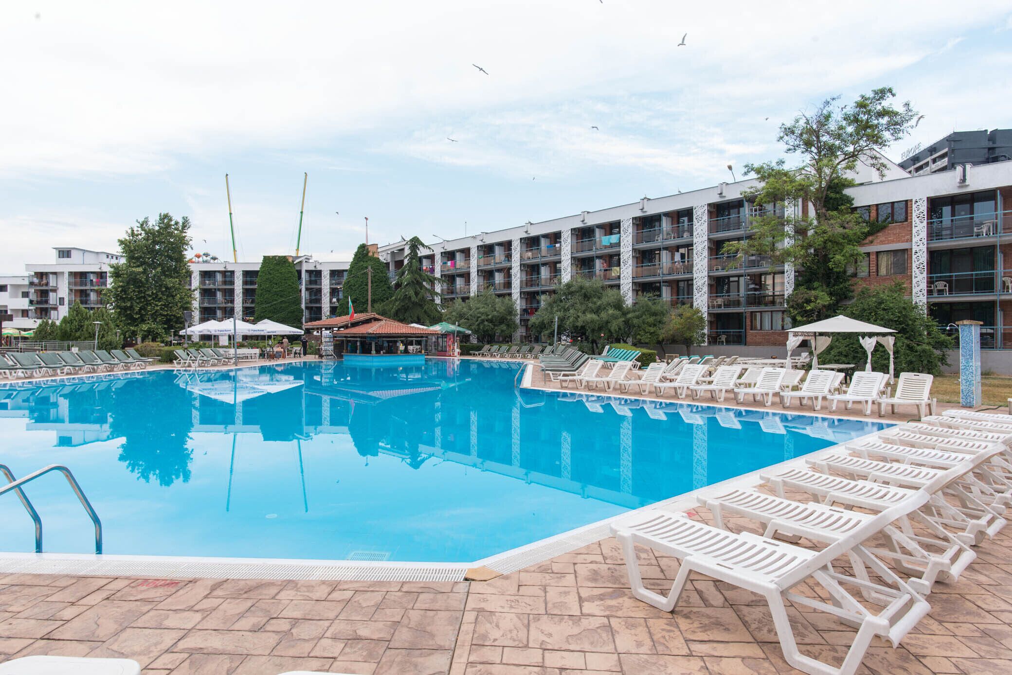 A swimming pool with lounge chairs and umbrellas, surrounded by multi-story buildings with balconies.