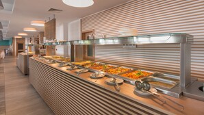 Un'area buffet con diverse postazioni gastronomiche, vassoi d'acciaio inossidabile e illuminazione a sospensione.