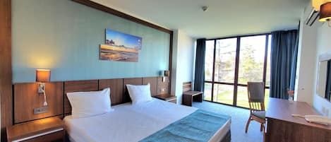 A hotel room with a large bed, a desk, a chair, a painting on the wall, and a window with curtains.