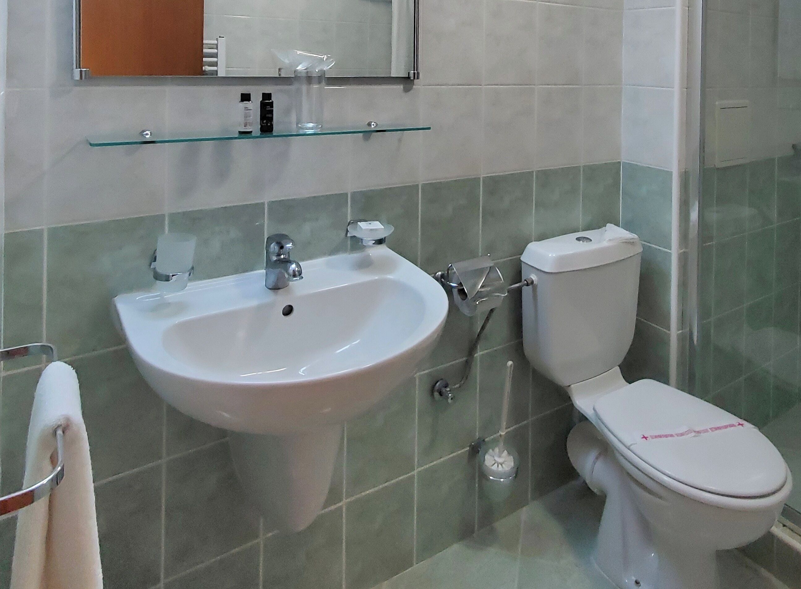 Un baño con lavamanos, inodoro y estante de vidrio sobre el lavamanos.