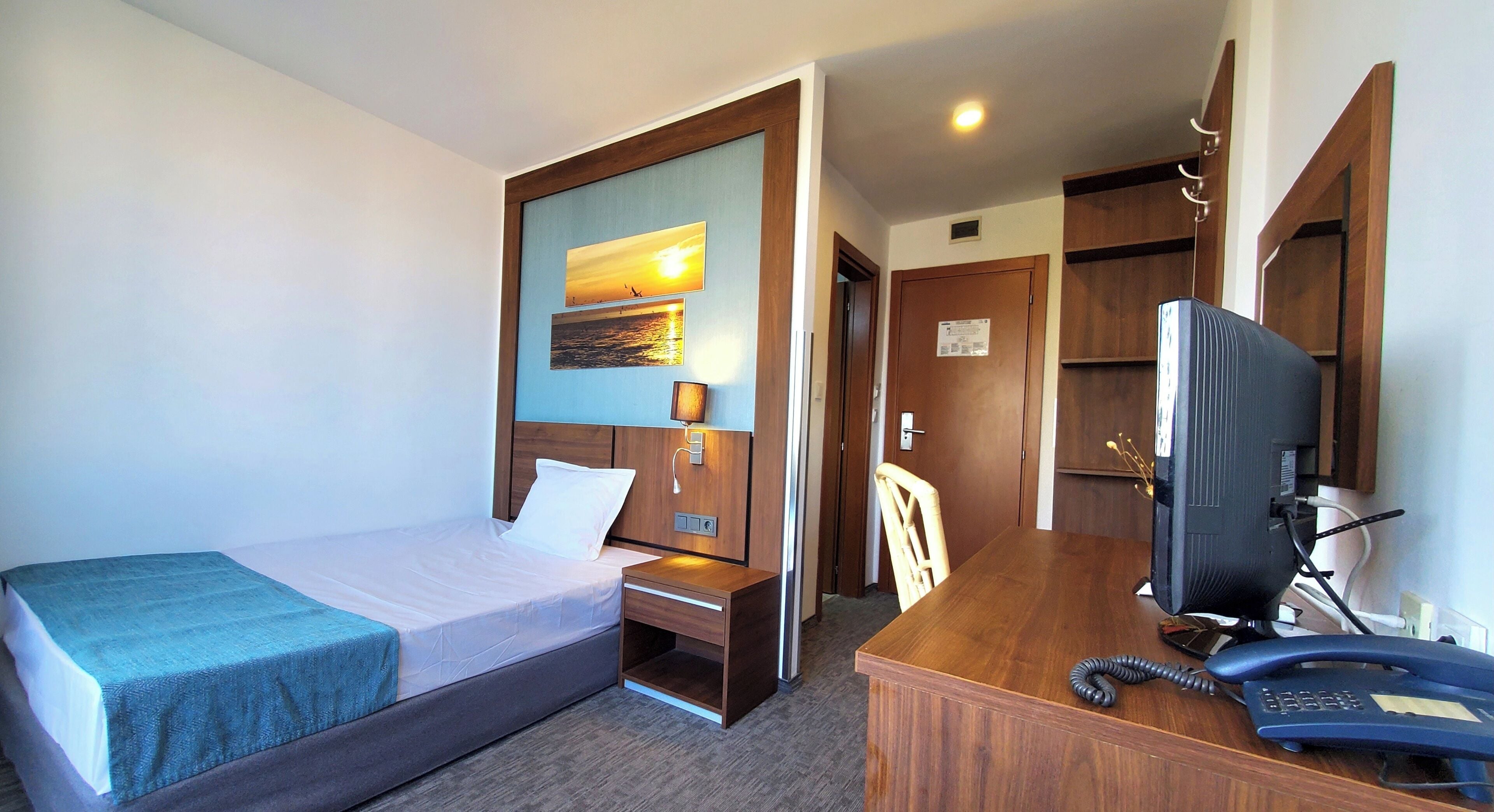 Una habitación de hotel con cama, escritorio, silla, televisor y un armario de madera.