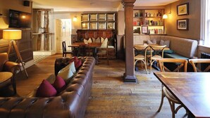 A cozy lounge area with a leather sofa, wooden tables, and chairs, a bookshelf, and a television.