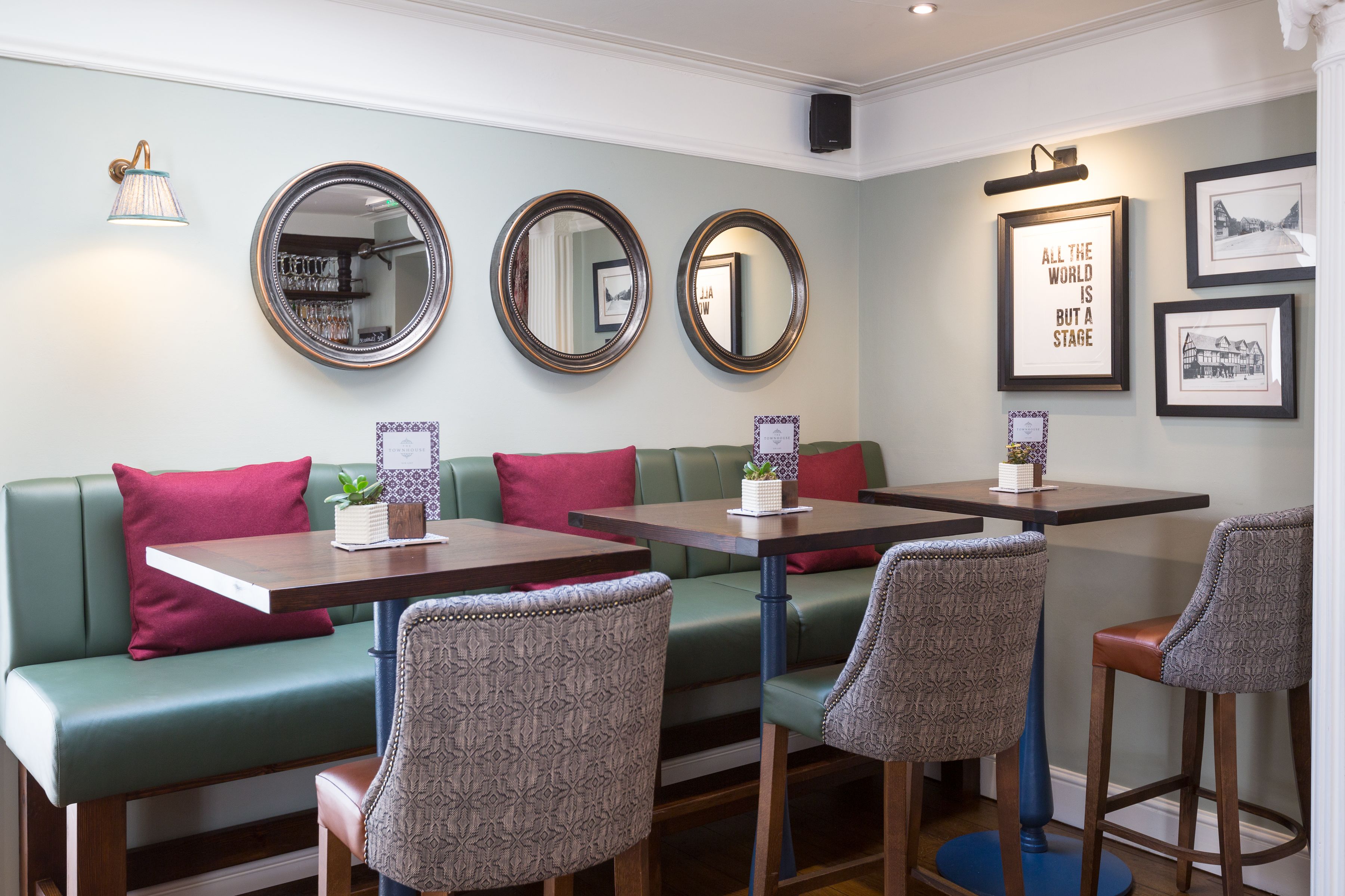 A restaurant with green cushioned seating, patterned chairs, and a wall with framed pictures and mirrors.