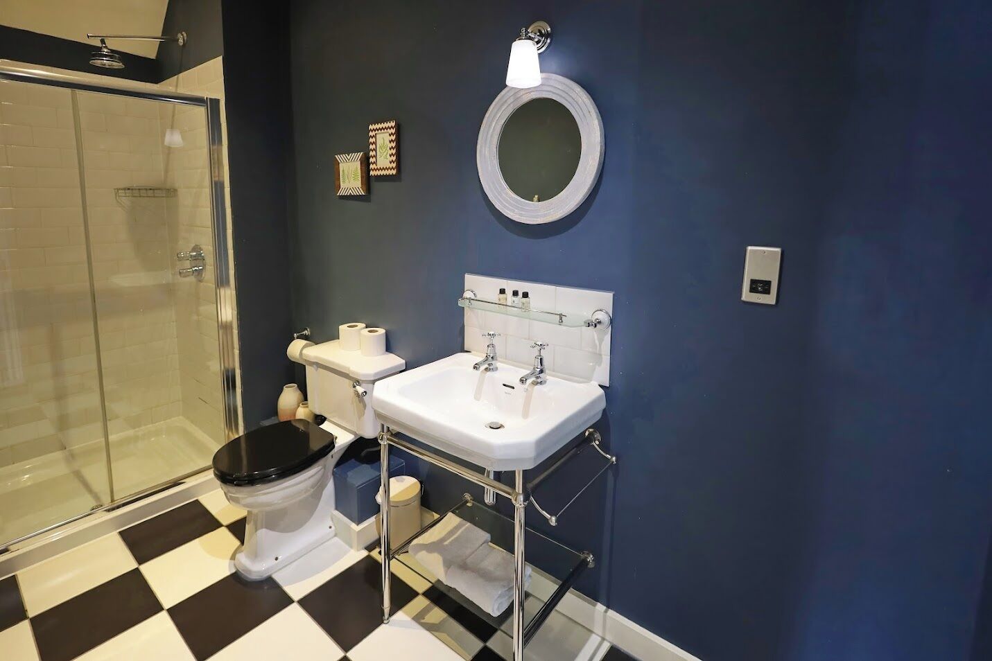 A bathroom with a black and white checkered floor, a white sink, a toilet, and a glass shower enclosure.