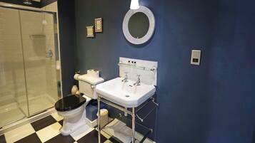 A bathroom with a black and white checkered floor, a white sink, a toilet, and a glass shower enclosure.