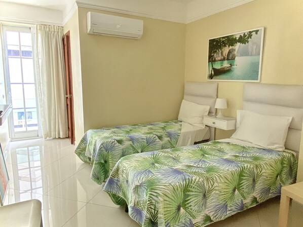 Habitación de hotel con dos camas, un cuadro, aire acondicionado y vistas al exterior.