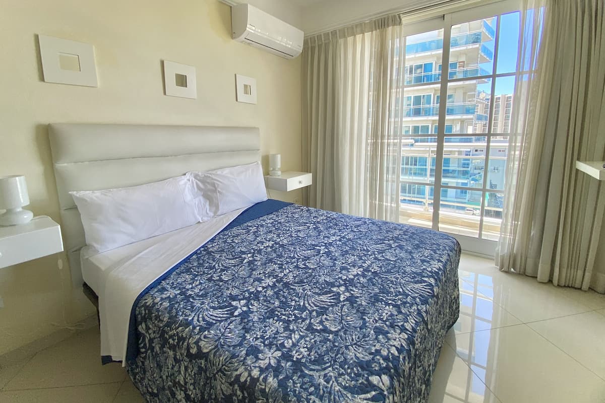 Une chambre d’hôtel équipée d’un lit, d’une table de chevet, d’un appareil de climatisation et d’une fenêtre avec des rideaux.
