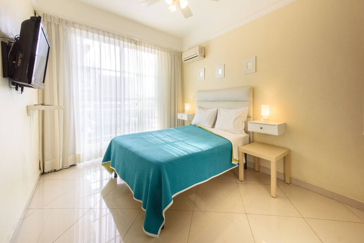 Une chambre d’hôtel avec un lit, des tables de chevet, une télévision et une fenêtre avec des rideaux.