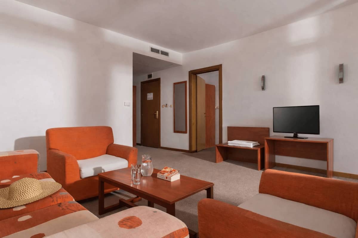 Habitación de hotel con sofá, sillón, televisión y una mesita con un control remoto.